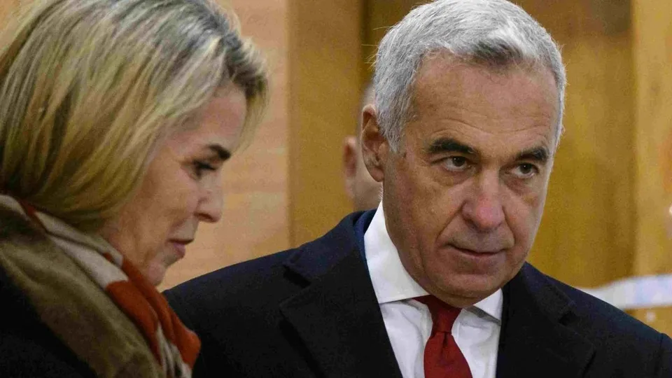 Un bărbat cu părul cărunt și cravată roșie stă lângă o femeie cu părul blond și eșarfă maro.