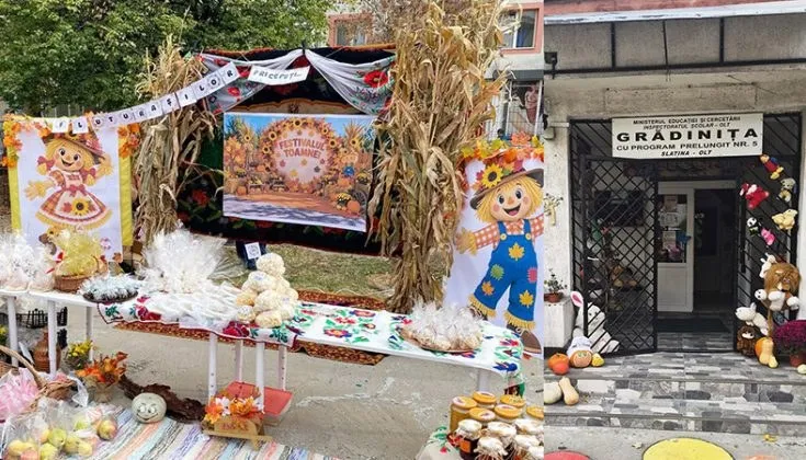 Un masa lungă acoperită cu o față de masă decorată este așezată în fața unei clădiri, fiind încărcată cu diverse fructe și decorațiuni de toamnă.