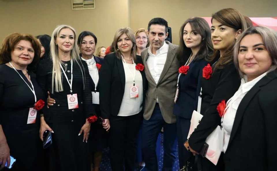 Un grup de persoane îmbrăcate în haine negre și albe stau grupate pentru o fotografie într-un spațiu interior.
