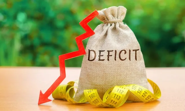 Un sac de pânie cu textul DEFICIT, o sărmă de măsură galbenă și o săgeată roșie care indică în jos pe o suprafață plană.