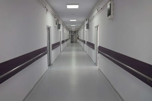 Un coridor lung cu pereți albi, o bandă purpurie pe ambele părți și lumini rectangulare în tavan.