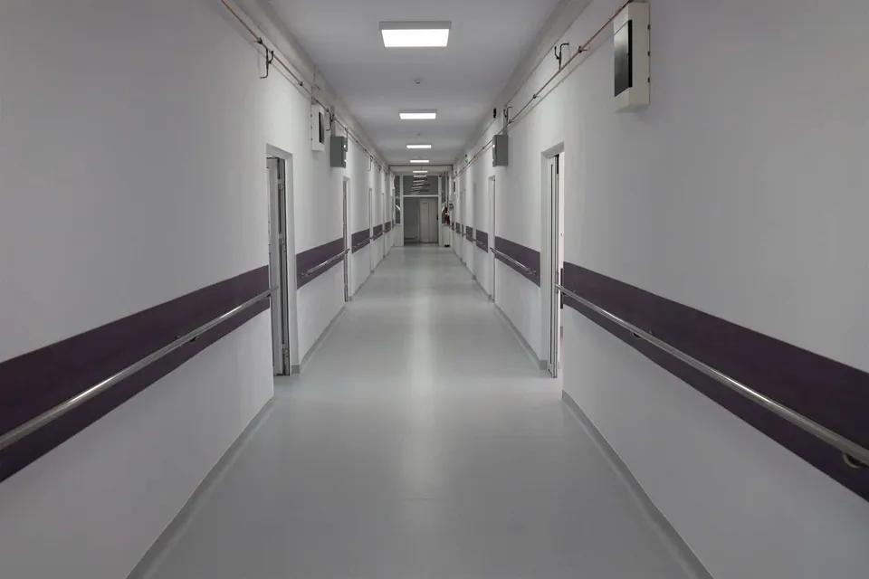 Un coridor lung cu pereți albi, o bandă purpurie pe ambele părți și lumini rectangulare în tavan.