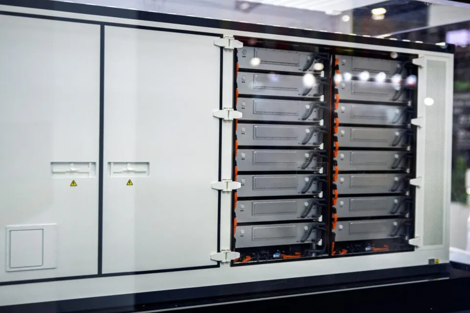 Un container alb cu panouri deschise dezvăluie rânduri de module gri de stocare a energiei așezate în interiorul unui suport metalic.