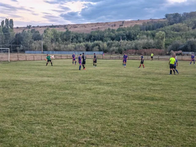 Câțiva jucători de fotbal în echipamente colorate sunt împrăștiați pe un teren de gazon verde sub un cer înnorat.