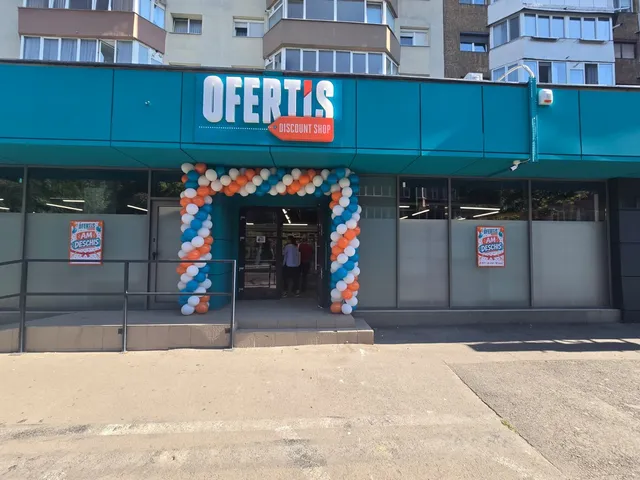 O clădire cu un panou albastru pe care scrie Ofertis Discount Shop este decorată cu un arc de baloane albe și albastre la intrare.