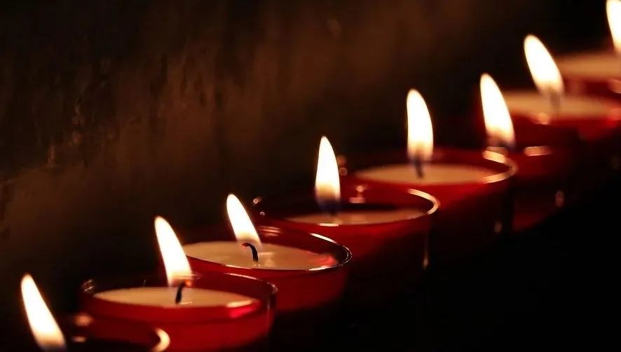 Mai multe lumânări aprinse sunt așezate într-un rând pe un fundal întunecat.