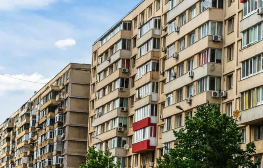 Blocuri de locuințe înalte cu numeroase balcoane închise și unități de aer condiționat montate pe fațade sub un cer cu nori dispersi.