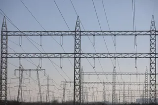 Mai multe turnuri de înaltă tensiune cu linii electrice suspendate se ridică sub un cer de seară.