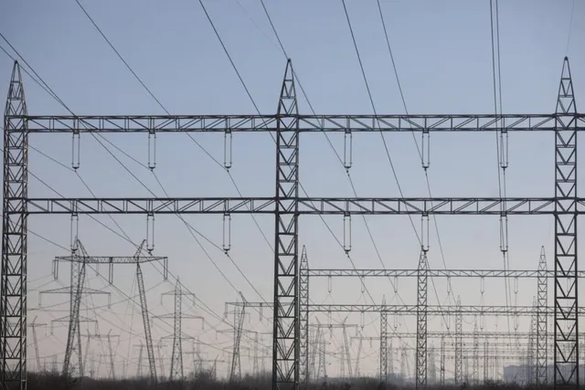 Mai multe turnuri de înaltă tensiune cu linii electrice suspendate se ridică sub un cer de seară.