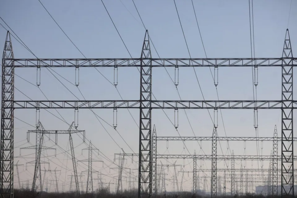 Mai multe turnuri de înaltă tensiune cu linii electrice suspendate se ridică sub un cer de seară.