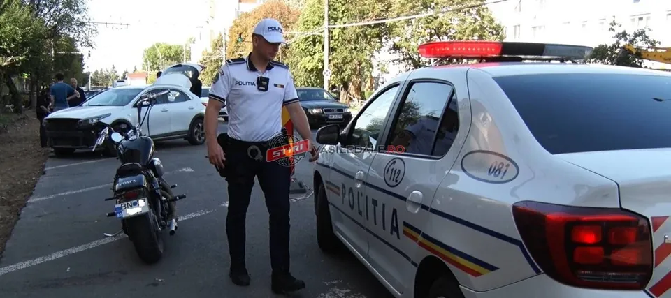Un polițist stă lângă o mașină de serviciu albă lângă o motocicletă neagră parcată pe un drum asfaltat.