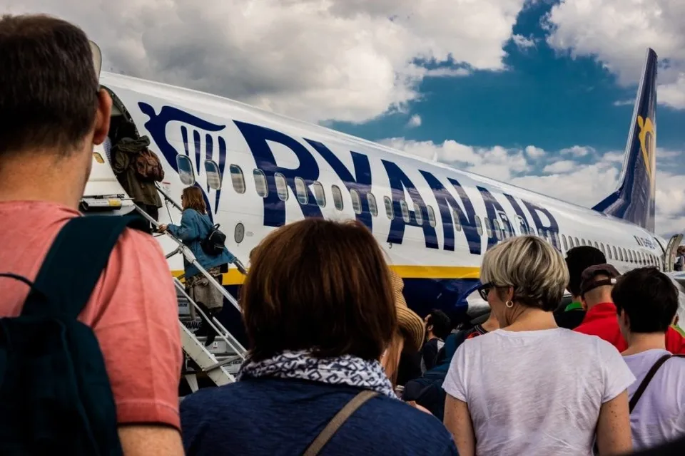Oamenii stau în coadă în fața unui avion alb cu inscripția RYANAIR sub un cer cu nori.