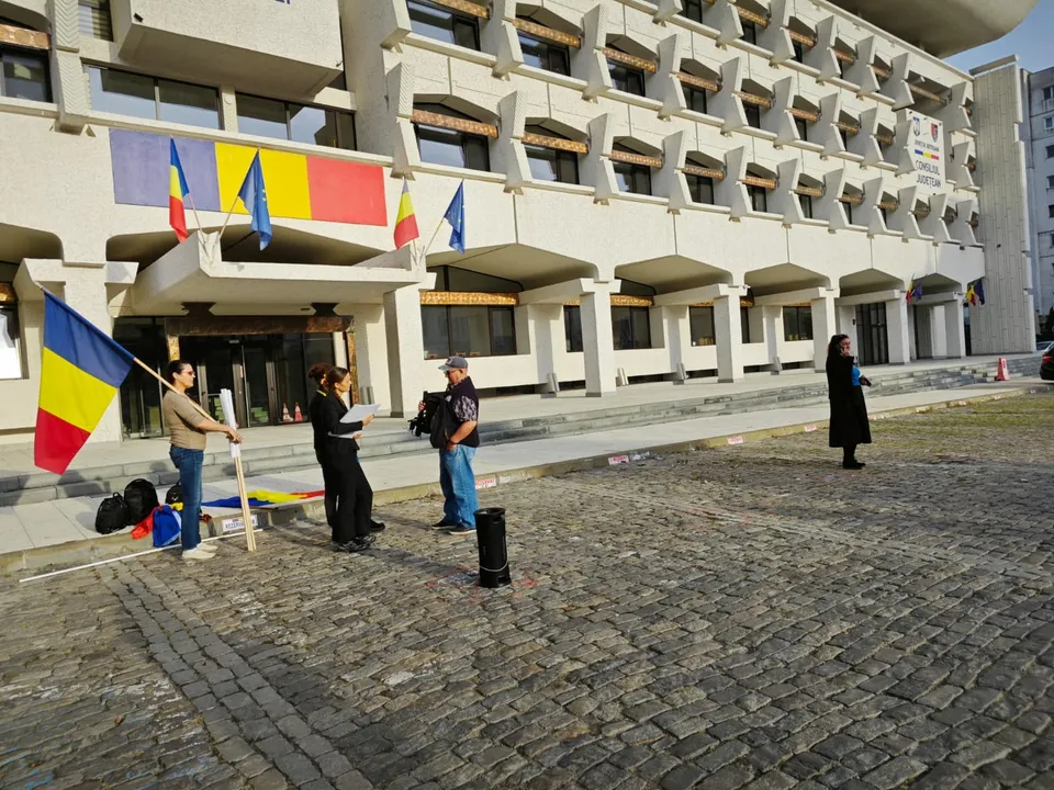 Patru persoane stau pe o piață pavată în fața unui clădire înaltă, una dintre ele ținând un steag tricolor.