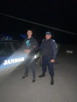 Un bărbat cu hanorac negru și un agent de jandarm în uniformă albastră stau lângă un vehicul de serviciu noaptea.