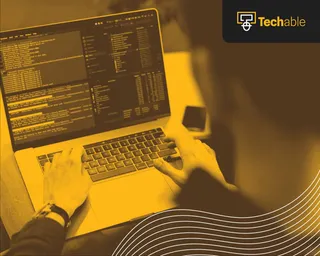 O persoană folosește un laptop pe care este afișat cod pe ecran, într-o lumină galbenă.