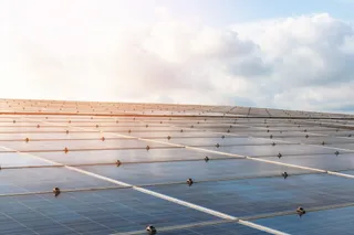 Rânduri de panouri fotovoltaice sunt instalate pe un teren sub un cer înconjurat de nori și lumină solară.