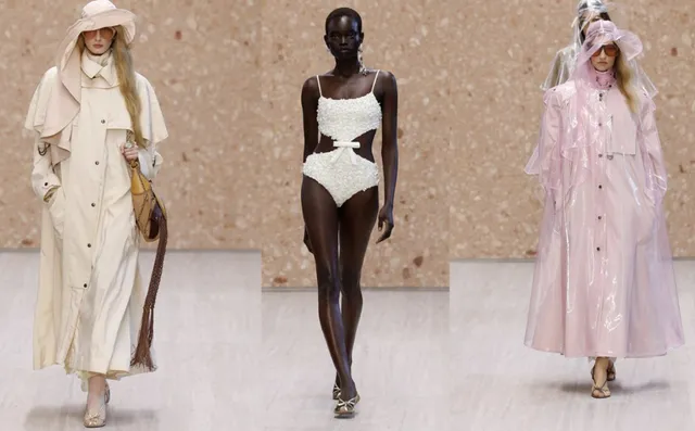 Trei modele merg pe o pistă de catwalk purtând haine de culoare crem, alb și roz pal, incluzând o rochie de baie și două trenchuri.