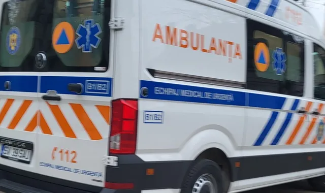 Un vehicul alb de tip ambulanță cu inscripții portocalii și albastre este parcat pe o stradă.