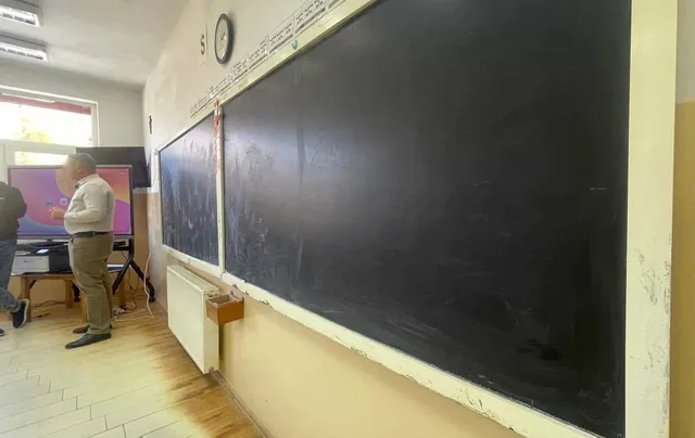 O tablă neagră mare este montată pe un perete al unei încăperi lângă un radiator și un monitor de tip ecran plat.