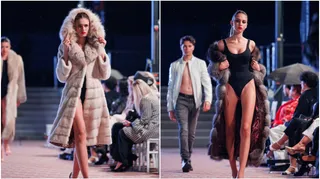 Patru modele defilează pe o pistă de catwalk, purtând diverse haine, în timp ce un public stă așezat pe scaune în fundal.