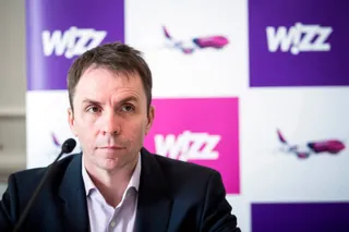Un bărbat cu părul scurt și cămașă deschisă la guler stă în fața unui panou cu logourile Wizz Air.