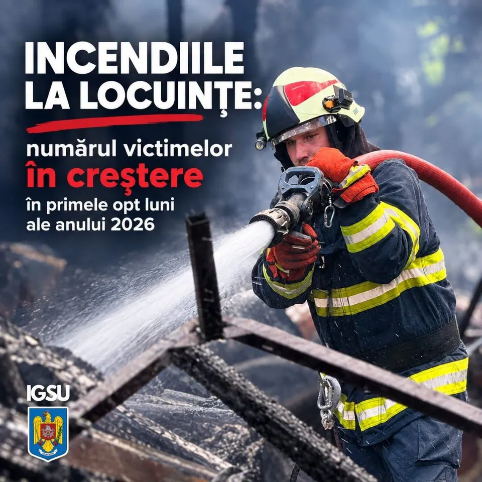 Un pompier cu cască și echipament de protecție pulverizează un jet de apă dintr-un furtun peste resturi carbonizate.