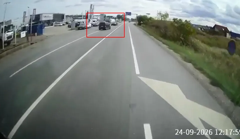 O perspectivă de pe un drum asfaltat cu linii albe marcate arată două autoturisme circulând pe o bandă de rulare sub un cer înnorat.