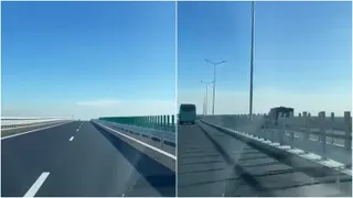 O porțiune de autostradă cu benzi marcate și bariere metalice de protecție sub un cer senin.