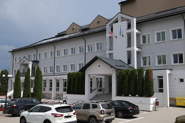 O clădire gri cu ferestre albe, având un pridvor cu acoperiș înclinat și mașini parcate în fața acesteia.