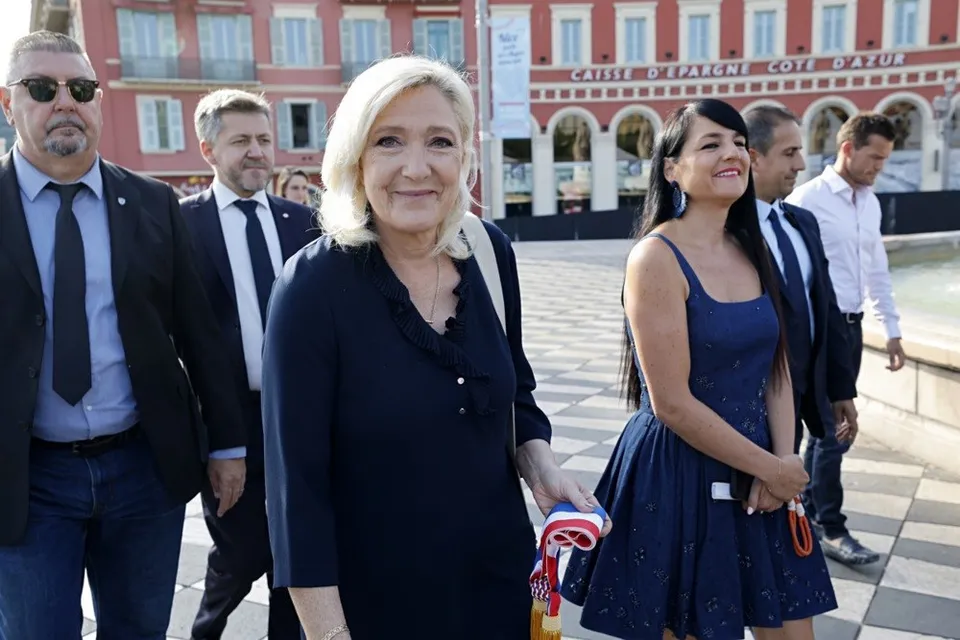Un grup de persoane merge pe o suprafață pavată în fața unei clădiri cu ferestre și arcade.