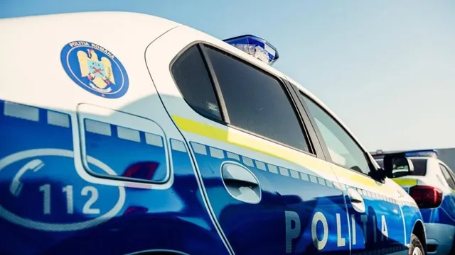 Un vehicul de poliție albastru și alb cu inscripția POLITIA și numărul 112 este parcat sub un cer senin.