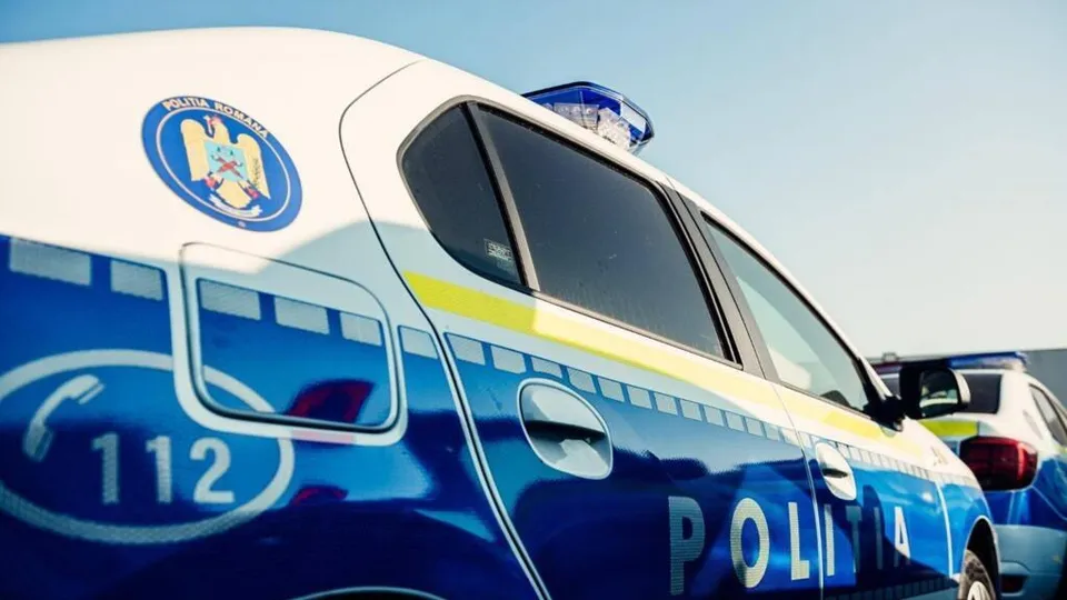Un vehicul de poliție albastru și alb cu inscripția POLITIA și numărul 112 este parcat sub un cer senin.