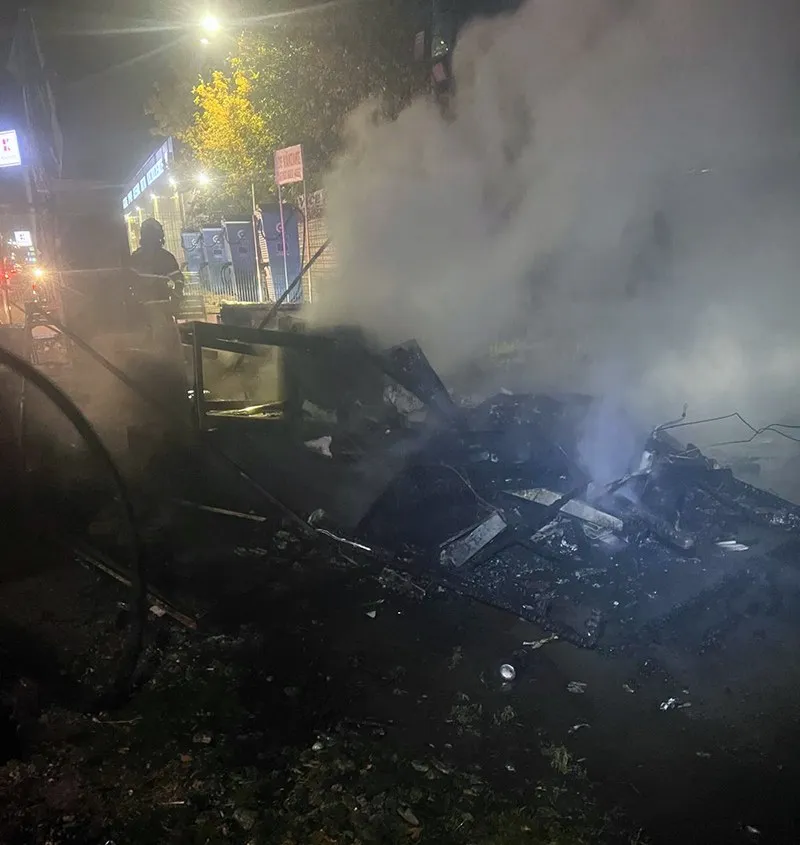 Un vehicul de tip rulotă este acoperit de fum dens și resturi carbonizate pe un teren întunecat noaptea.