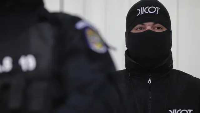 Un bărbat poartă o căciulă neagră cu inscripție albă și o mască neagră care îi acoperă fața.