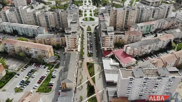 O vedere aeriană prezintă blocuri de locuințe dispuse în jurul unui spațiu verde central cu alei și mașini parcate în imediate apropiere.