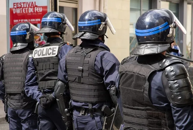 Patru polițiști în uniformă albastră și echipament de protecție negru stau cu spatele la cameră.