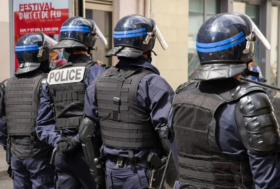 Patru polițiști în uniformă albastră și echipament de protecție negru stau cu spatele la cameră.
