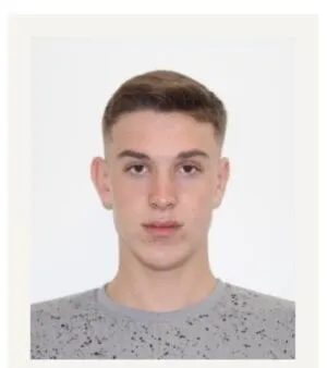 Un bărbat tânăr cu părul scurt și deschis la culoare poartă un tricou gri cu modele punctate pe un fundal alb.
