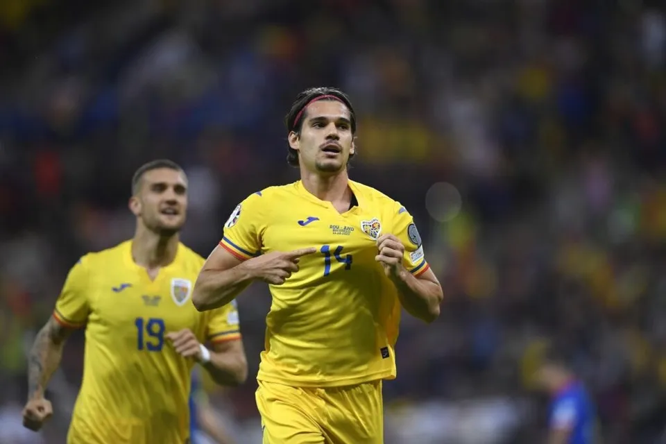 Un jucător de fotbal în echipament galben cu numărul 14 indică spre pieptul său, fiind urmat de un alt jucător în echipament similar.