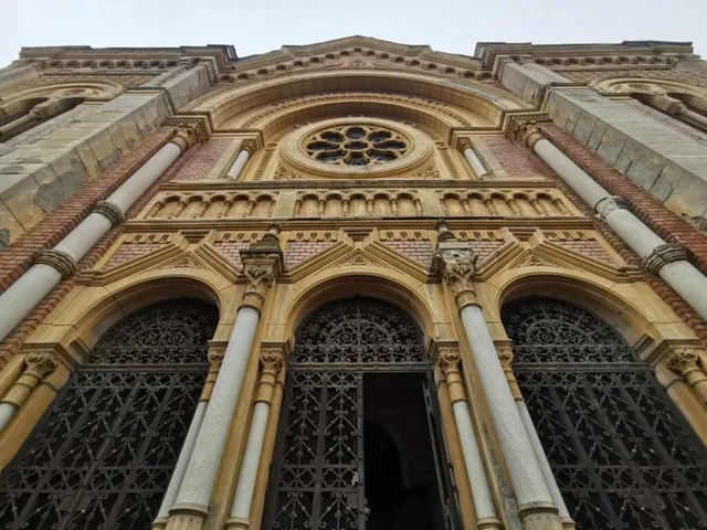Privire de jos a unei fațade de clădire din piatră cu trei arcade, coloane albe și un oculus circular decorat.