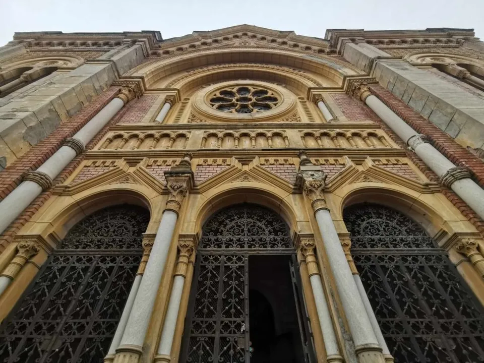 Privire de jos a unei fațade de clădire din piatră cu trei arcade, coloane albe și un oculus circular decorat.