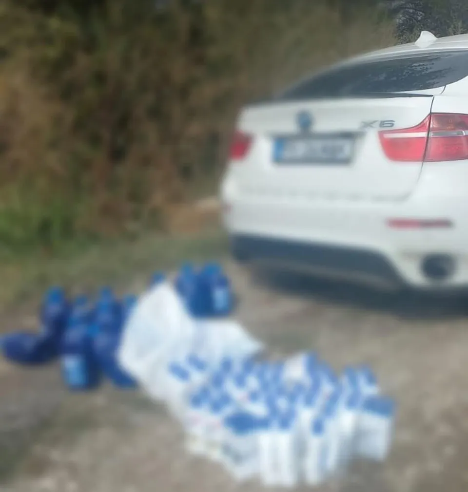 Un autovehicul alb este parcat pe un teren de lângă diverse recipiente și flacoane de culoare albastră așezate pe sol.