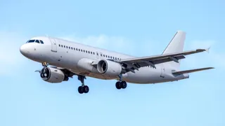 Un avion de pasageri alb zboară pe un cer albastru cu câteva nori, având trenul de aterizare extins.