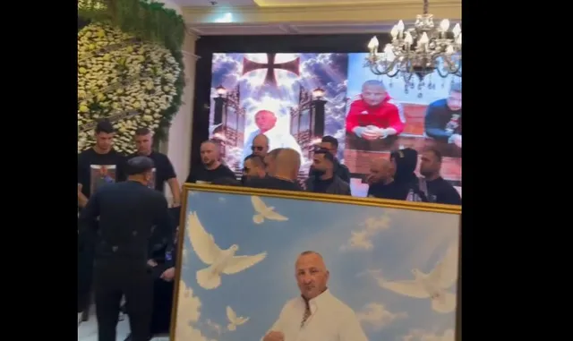 Un grup de bărbați stă în fața unui ecran mare care afișează imagini cu o cruce și un om, lângă un cadru cu porți albe.