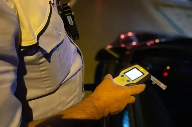 O persoană în uniformă ține un dispozitiv electronic cu un ecran luminos și un tub de suflare într-o zonă întunecată.