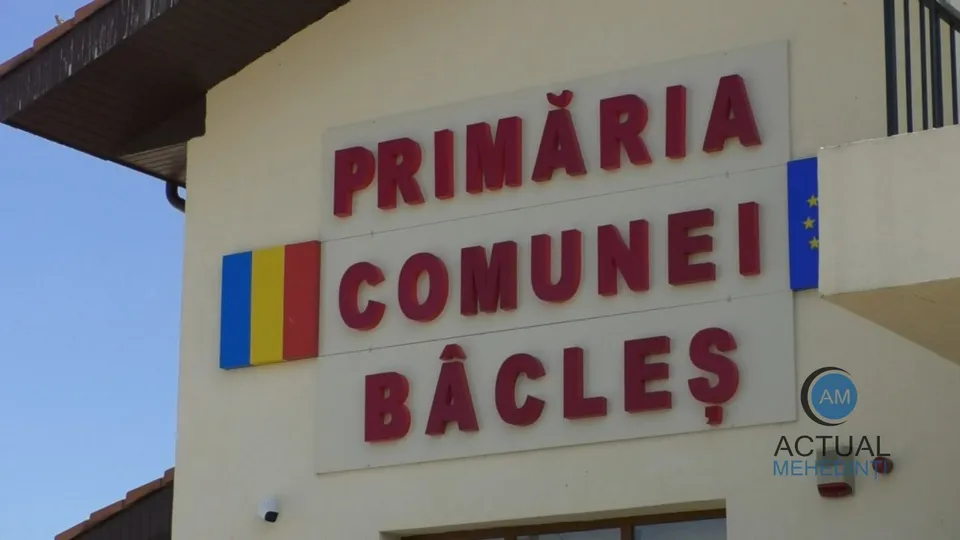 Un panou alb cu litere roșii pe o clădire indică Primăria Comunei Bâcleș, având drapele pe margini.