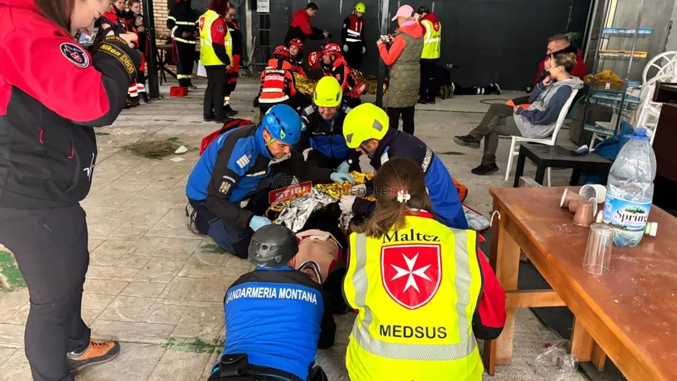 Mai mulți oameni în uniforme de salvator, unele cu cască și veste reflectorizante, lucrează împreună pe un teren pavat lângă o masă de lemn.