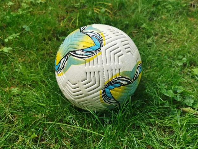 Un fotbal alb cu modele albastre și galbene este așezat pe un teren de iarbă verde.