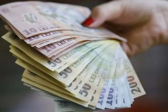 O mână cu unghiile vopsite în roșu ține un evantai de bancnote de lei românești de diferite valori.