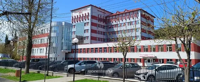 O clădire mare, albă cu dungi roșii, este înconjurată de copaci și are un parc de mașini în prim-plan.